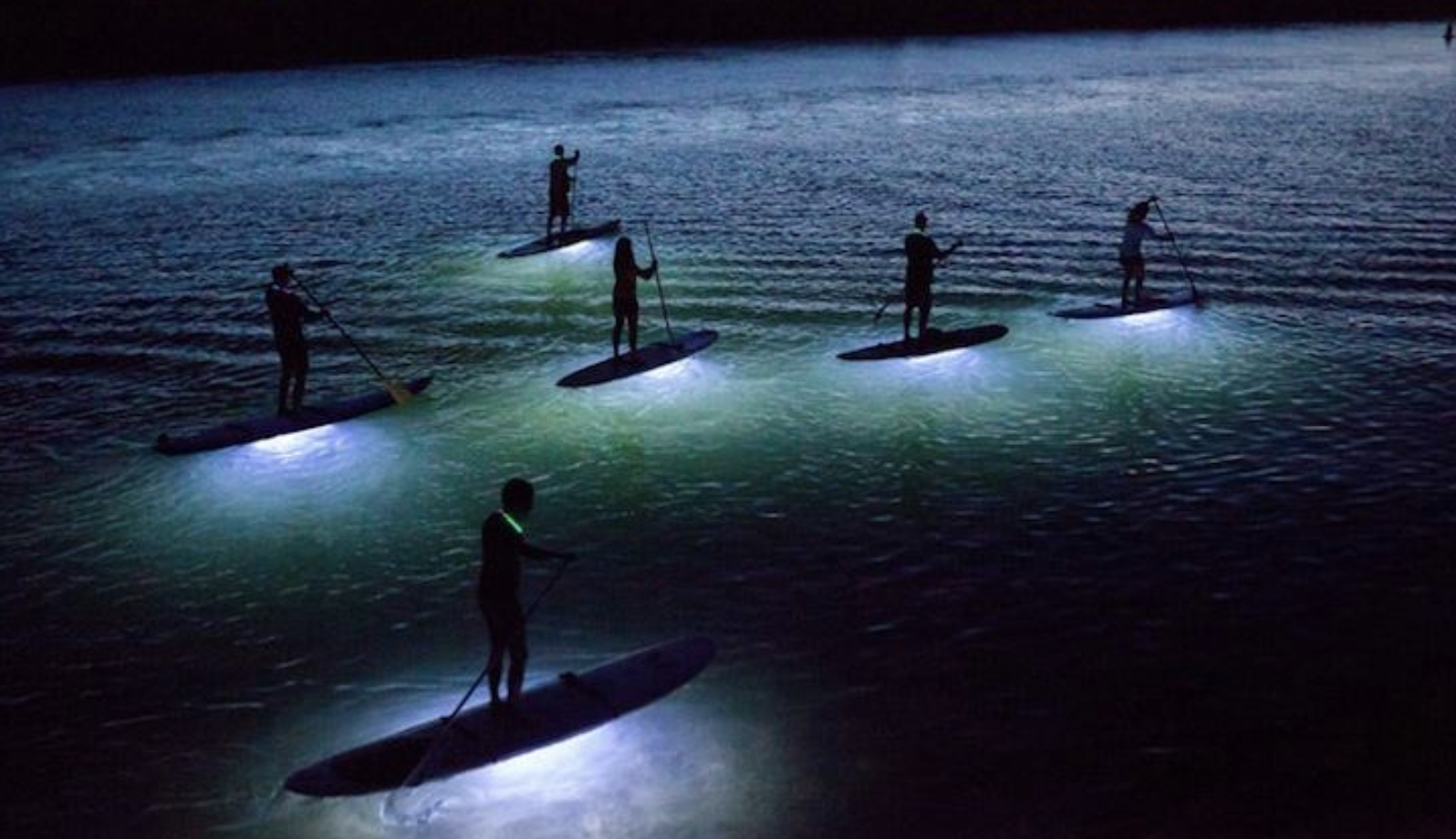 Skupina na osvětlených paddleboardech při noční plavbě po jezeře Milada